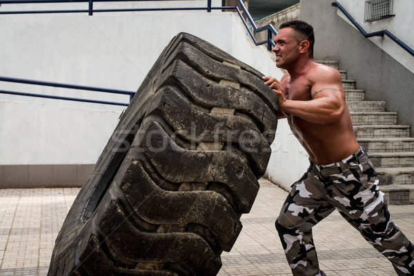 A muscular man participating in a cross fit workout by doing a tire flip Stock photo © Jasminko
