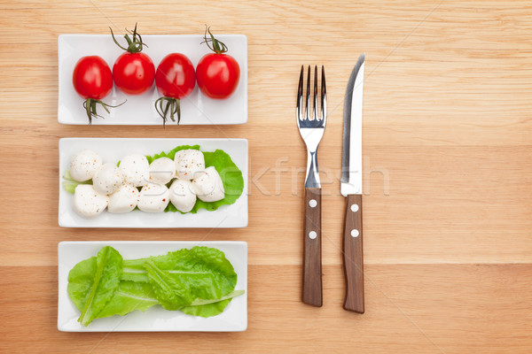 Tomatoes, mozzarella, green salad leaves and silverware Stock photo © karandaev