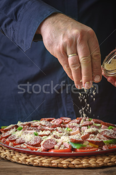 Man in a blue shirt sprinkle with cheese pizza on the table Stock photo © Karpenkovdenis