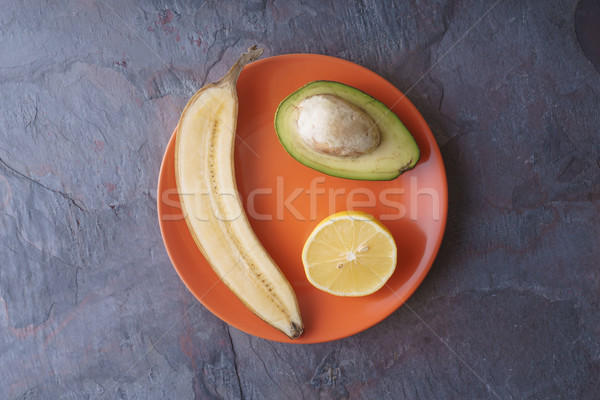 Avocado, lemon, banana halves lie on an orange plate on a slate Stock photo © Karpenkovdenis