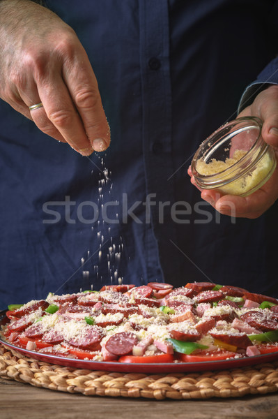 Man in a blue shirt sprinkle with cheese pizza from a sauser Stock photo © Karpenkovdenis