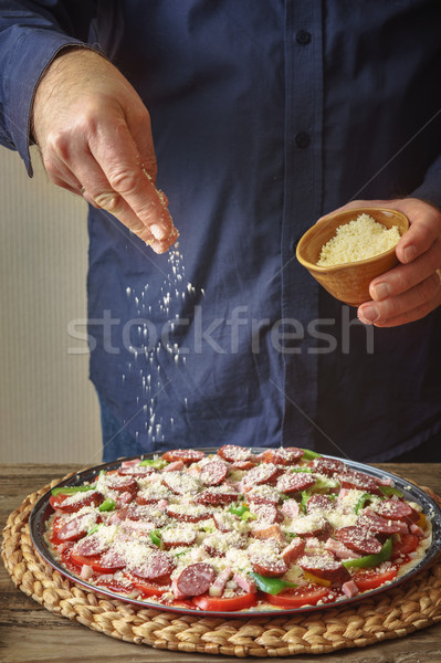 Man in a blue shirt sprinkle with cheese pizza from a ceramic sauser Stock photo © Karpenkovdenis