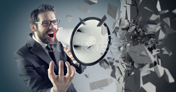 Young businessman crushing concrete wall with a megaphone Stock photo © konradbak