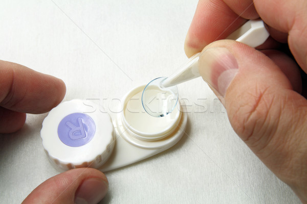 Stock photo:  Hand with tweezers and contact lens