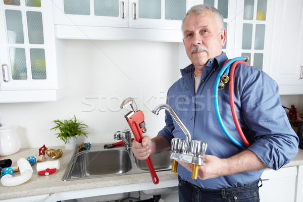 Stock photo: Plumber in kitchen with a wrench.