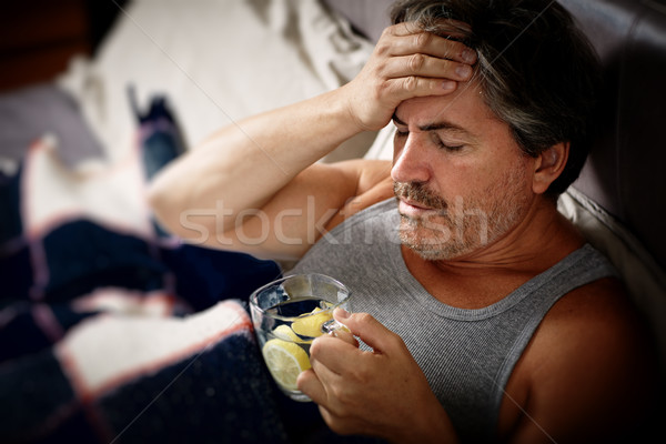 Sick man with fever in bed with cup lemon tea. Stock photo © Kurhan