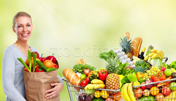 Stock photo: Young woman near shopping cart with food.