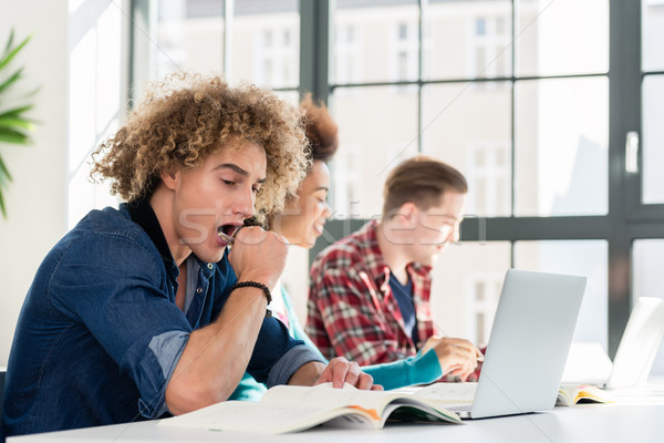 Funny student yawning in front of a book while sitting down at desk Stock photo © Kzenon