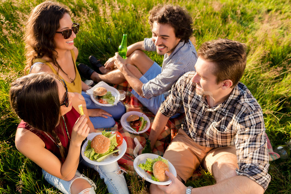 Friends sitting in grass and having burgers at barbecue party  Stock photo © Kzenon