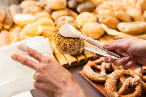 Sales woman in baker shop putting bread roll in paper bag Stock photo © Kzenon