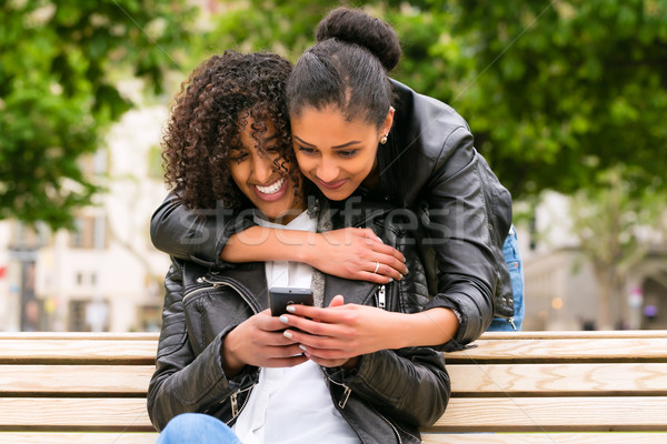 Best friends chatting with smartphone on park bench Stock photo © Kzenon