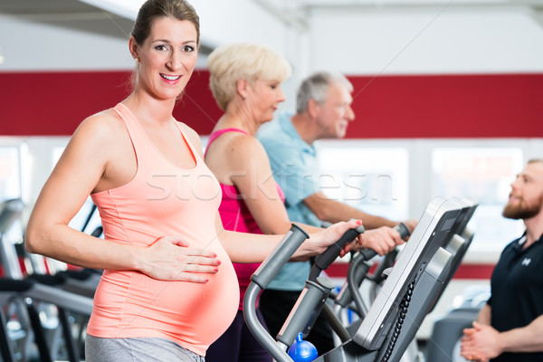 Pregnant woman on cross trainer at the gym touches her belly  Stock photo © Kzenon