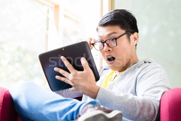 Young Asian man surprised by the online information displayed on a tablet PC Stock photo © Kzenon