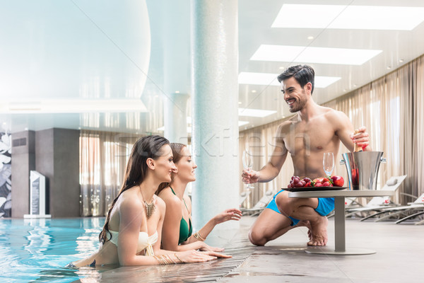 Young man serving with champagne two women at the swimming pool  Stock photo © Kzenon