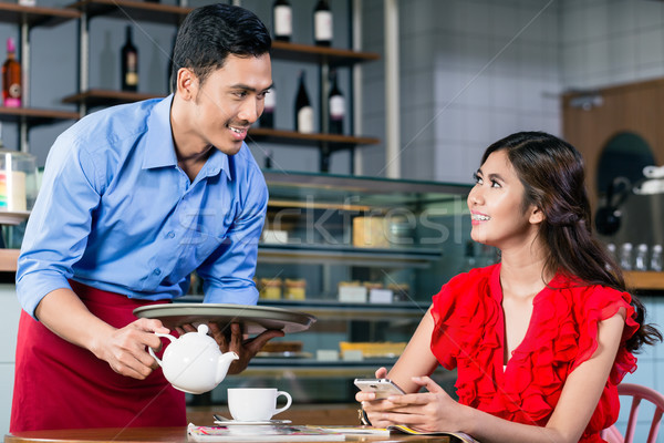 Handsome waiter flirting with a beautiful woman while serving coffee Stock photo © Kzenon