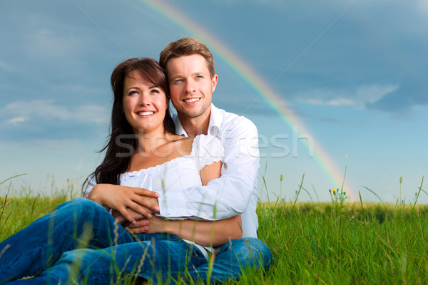 Happy couple sitting on a meadow under rainbow Stock photo © Kzenon