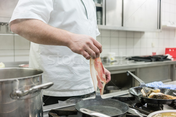 Stock photo: Chef putting ham into frying pan on stove in restaurant kitchen