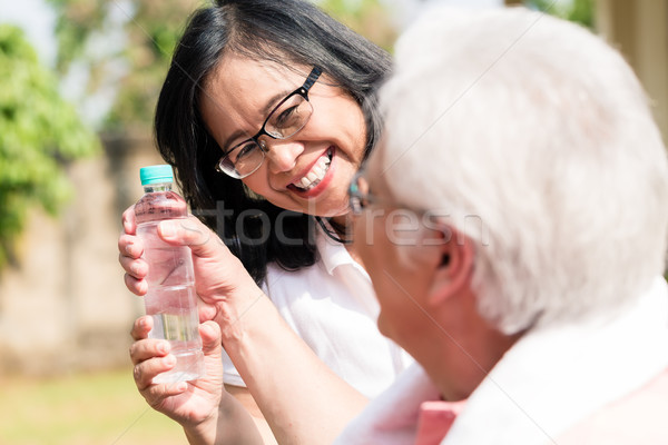 Careful senior woman giving a bottle of water to her partner out Stock photo © Kzenon