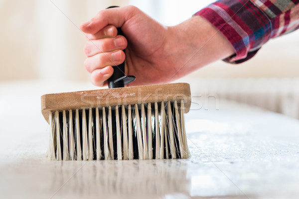Stock photo: Hand of a man holding a synthetic brush while applying paste to wallpaper sheet