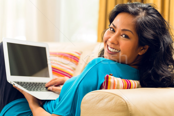 Stock photo: Asian Woman sitting on couch surfing the internet and smiling