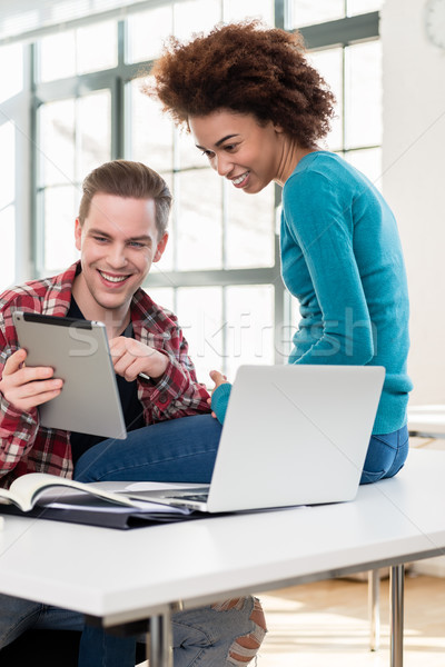 Stock photo: Two happy students watching a funny video on a tablet PC during break