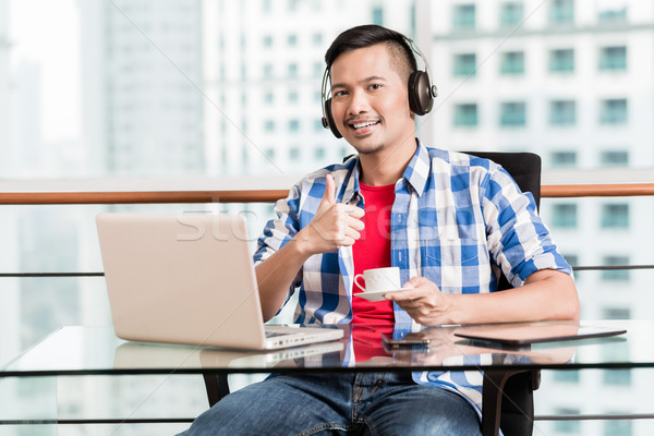 Young asian man in office having coffee giving thumbs up sign Stock photo © Kzenon