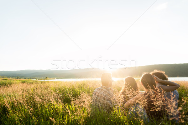 Friends sitting together at lake enjoying sunset Stock photo © Kzenon