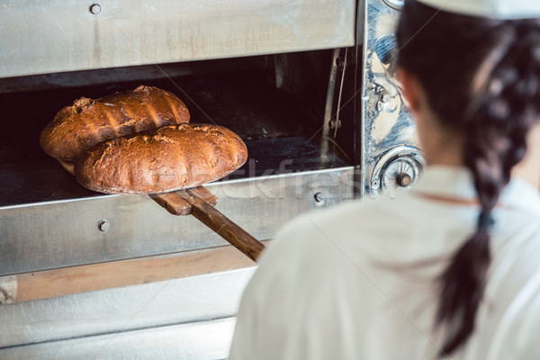 Stock photo: Baker getting fresh bread with shovel out of oven