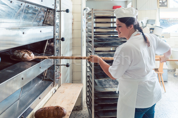 Baker woman getting bread out of bakery oven Stock photo © Kzenon