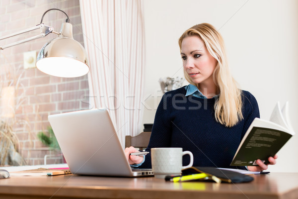 Stock photo: Woman holding book looking at laptop