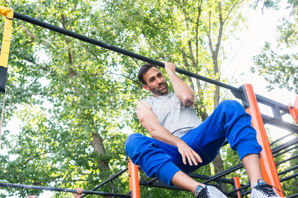 Powerful young man doing one-arm pull-ups while hanging on a bar in park Stock photo © Kzenon