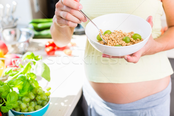 Terhes nő egészségesen enni müzli gyümölcs áll konyhapult Stock fotó © Kzenon