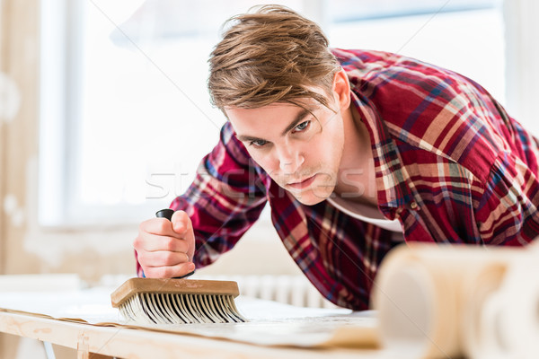 Young man applying paste to the surface of a wallpaper sheet dur Stock photo © Kzenon