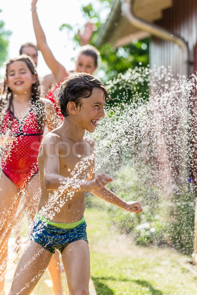 Boy cooling down with garden hose, family in the background Stock photo © Kzenon