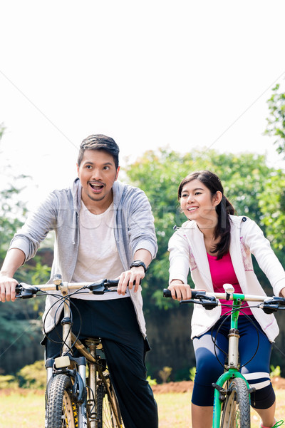 Young Asian couple laughing together while riding bicycles  Stock photo © Kzenon