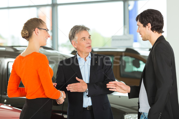 Mature man handshaking with young couple and auto in car dealership Stock photo © Kzenon