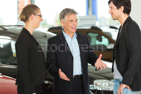 Mature man with young couple and autos in car dealership Stock photo © Kzenon