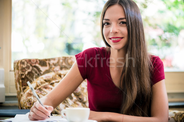 Young woman looking at camera while writing indoors Stock photo © Kzenon
