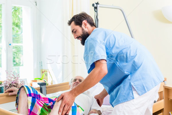 Elderly care nurse helping senior man from wheelchair to bed Stock photo © Kzenon