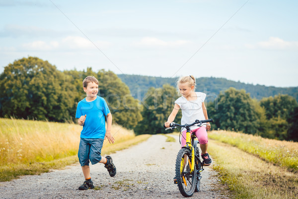 Boy and girl walking and riding bicycle on a dirt path Stock photo © Kzenon