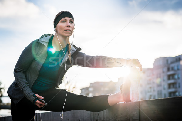 Young woman stretching her leg during outdoor warming up routine Stock photo © Kzenon