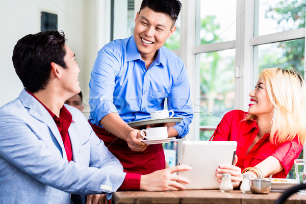 Friendly Asian waiter serving a couple coffee Stock photo © Kzenon