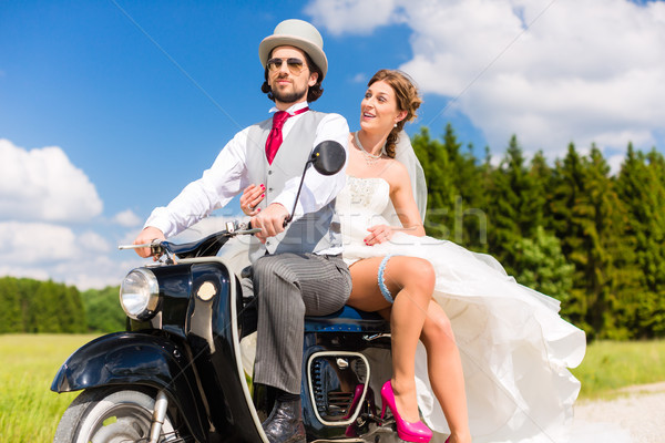 Bridal pair driving motor scooter wearing gown and suit Stock photo © Kzenon