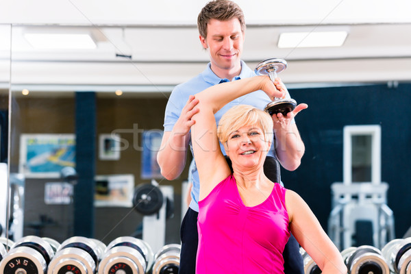 Senior woman at sport exercise in gym with trainer Stock photo © Kzenon