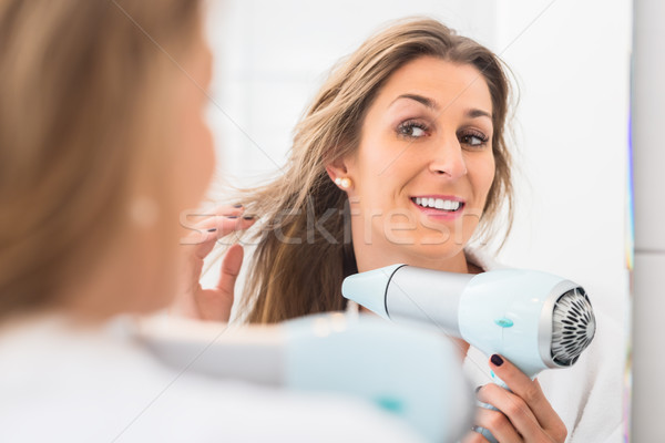 Woman blow drying her hair in front of mirror Stock photo © Kzenon