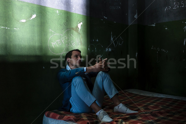 Depressed young man sitting on a mattress in a dark prison cell  Stock photo © Kzenon
