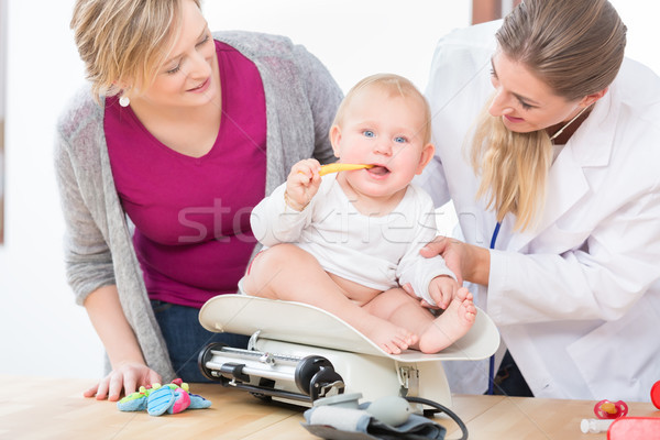 Pediatric care specialist smiling while measuring the weight of a baby girl Stock photo © Kzenon