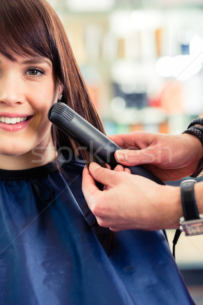 Male coiffeur dress women hair with flat iron in shop Stock photo © Kzenon