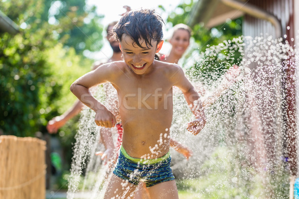Boy cooling down with garden hose, family in the background Stock photo © Kzenon