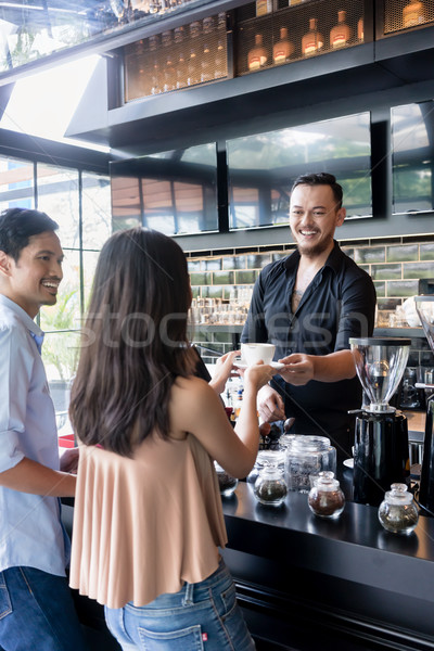 Cheerful bartender serving coffee over the bar counter to a youn Stock photo © Kzenon
